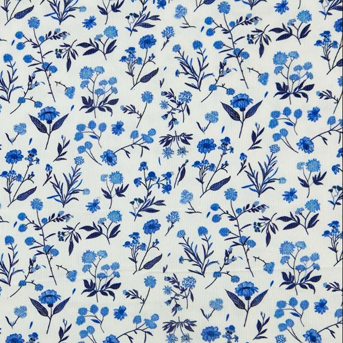 White cotton corduroy fabric with scattered blue floral motifs in various shades