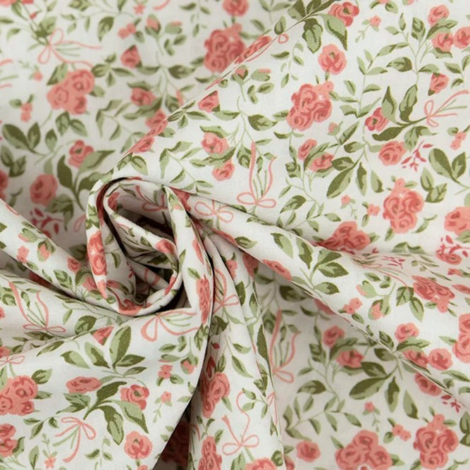 White cotton poplin fabric with pink roses, green leaves, and bow print pattern.