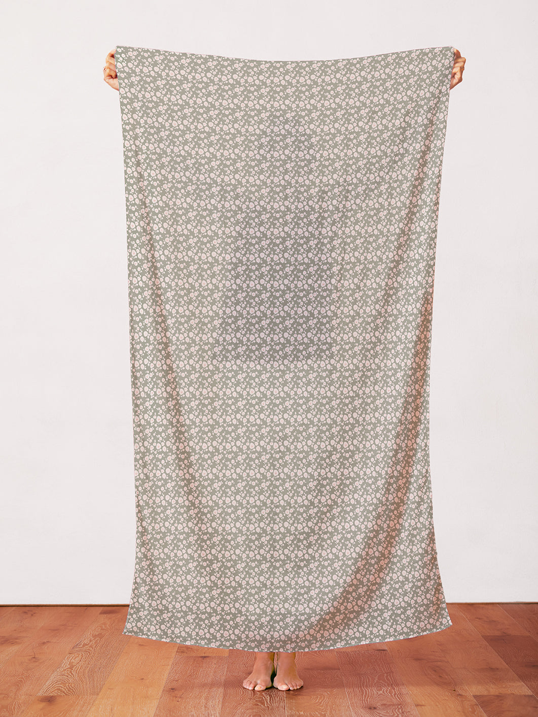 Sage green fabric with small white floral blossoms pattern, held up full length.