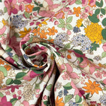 White cotton poplin fabric with pink, orange, yellow, and blue floral print, draped and twisted.