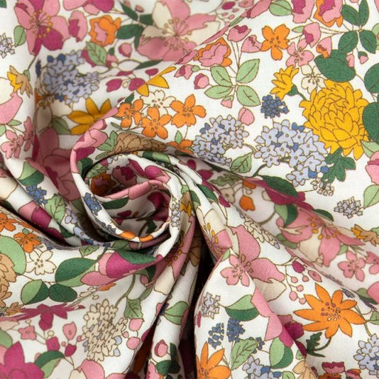 White cotton poplin fabric with pink, orange, yellow, and blue floral print, draped and twisted.