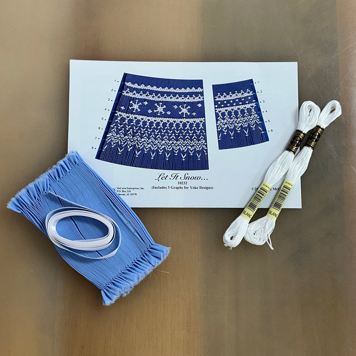 Let It Snow smocking kit with blue pleated fabric, white DMC floss, and pattern graph