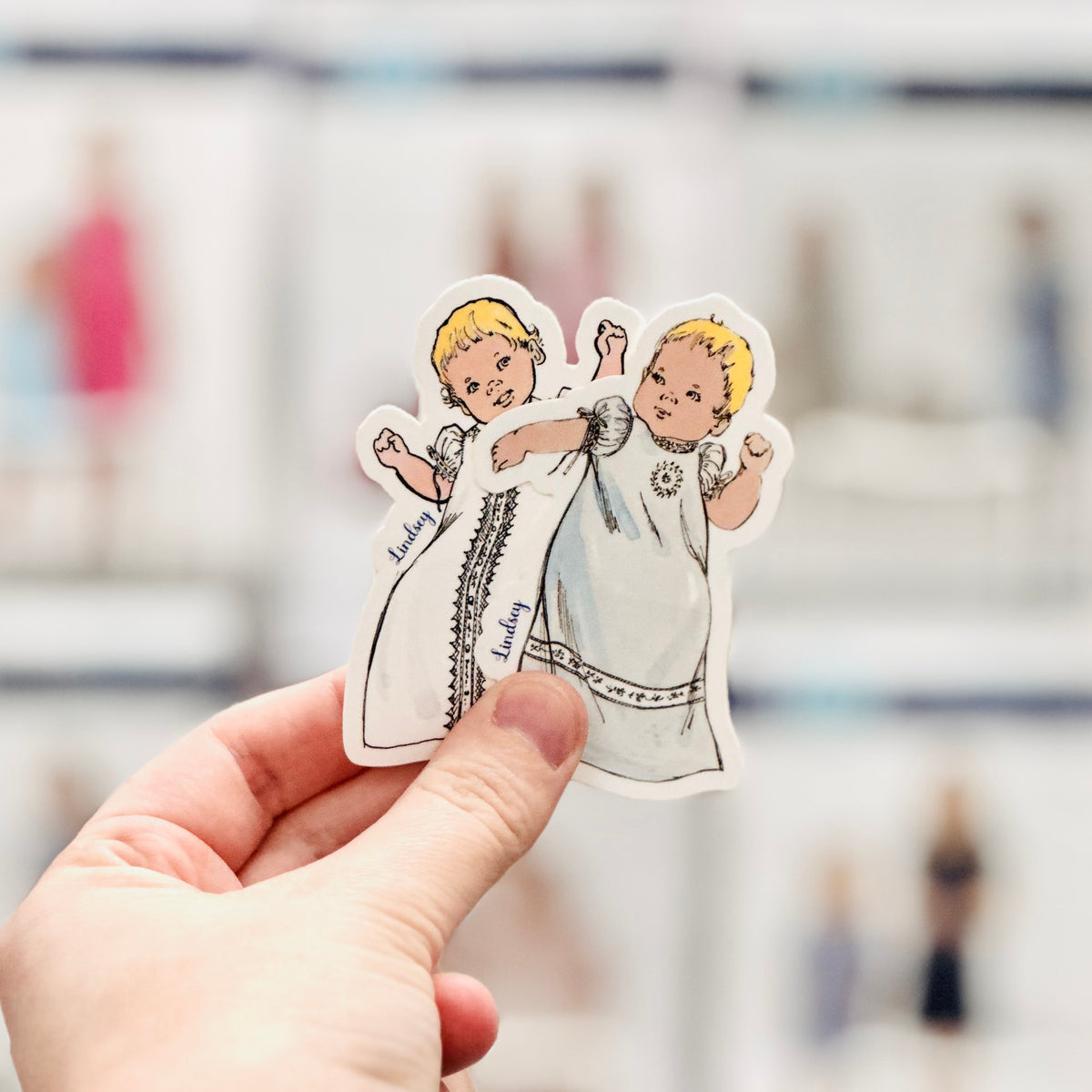 Vintage-style sticker of two blonde toddlers in white christening gowns labeled Lindsey