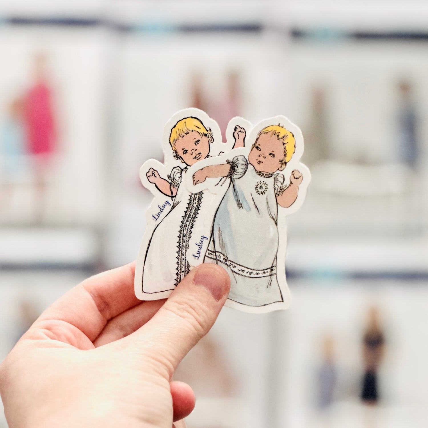 Vintage-style sticker of two blonde toddlers in white christening gowns labeled Lindsey
