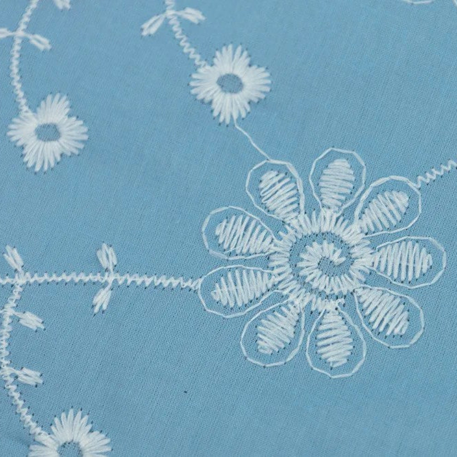 Close-up of sky blue fabric with white embroidered daisy vine eyelet pattern
