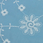 Close-up of sky blue fabric with white embroidered daisy vine eyelet pattern