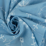Sky blue cotton eyelet fabric with white embroidered daisy vine floral pattern, swirled detail shot