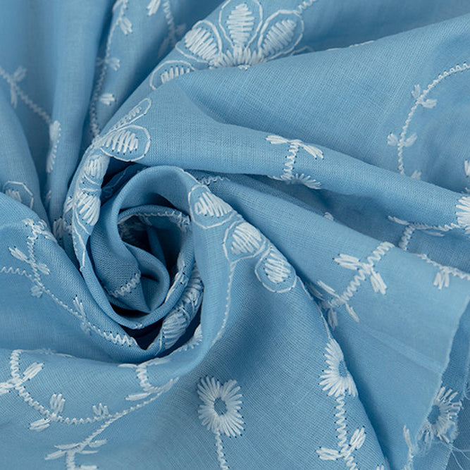 Sky blue cotton eyelet fabric with white embroidered daisy vine floral pattern, swirled detail shot