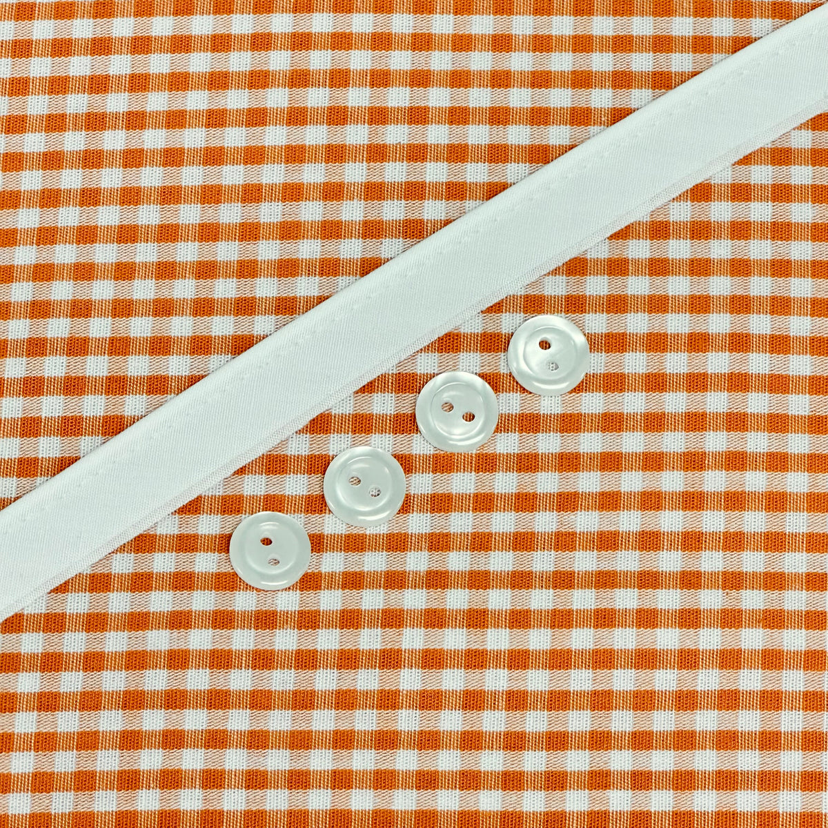 Orange gingham fabric with white ribbon trim and four pearl buttons