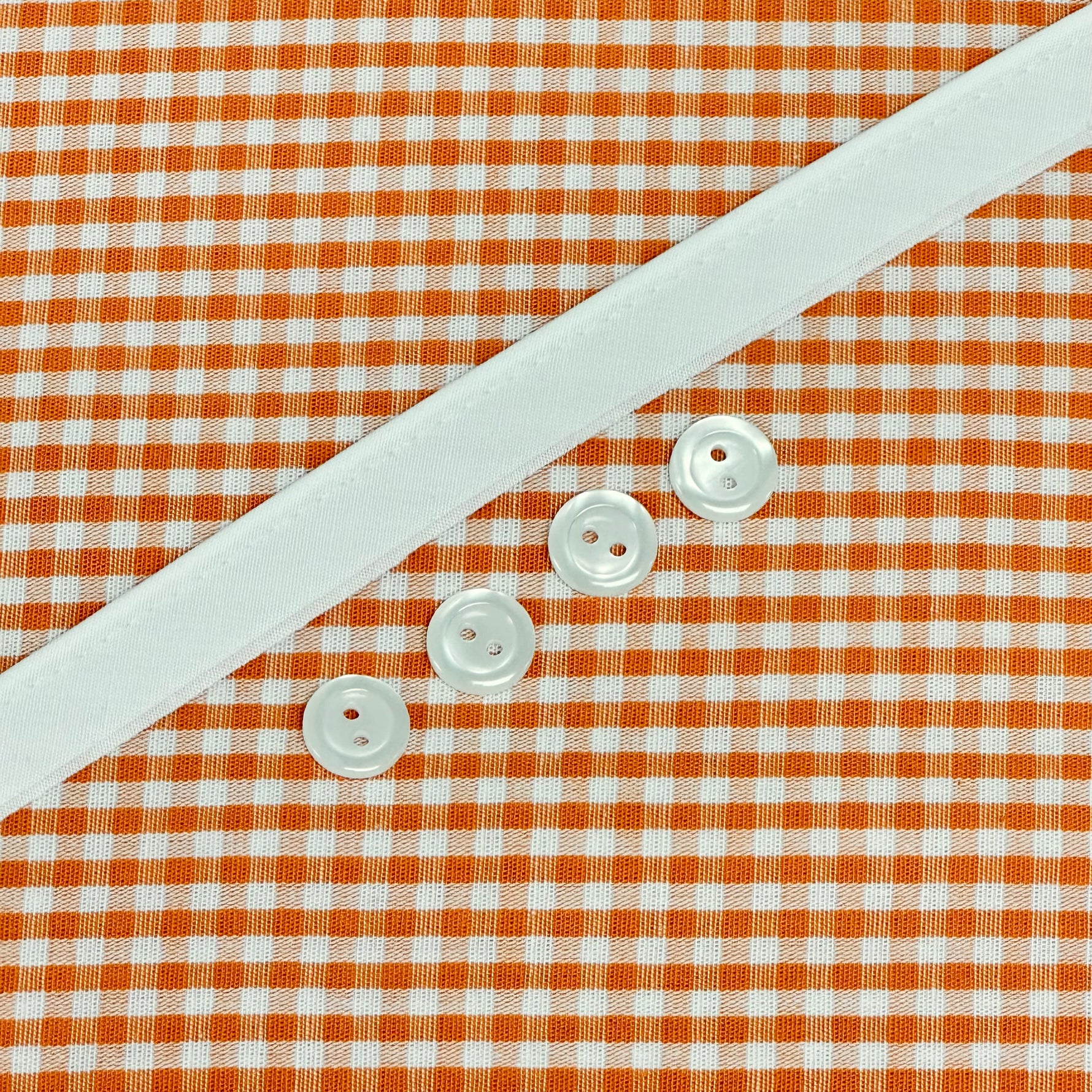 Orange gingham fabric with white ribbon trim and four pearl buttons