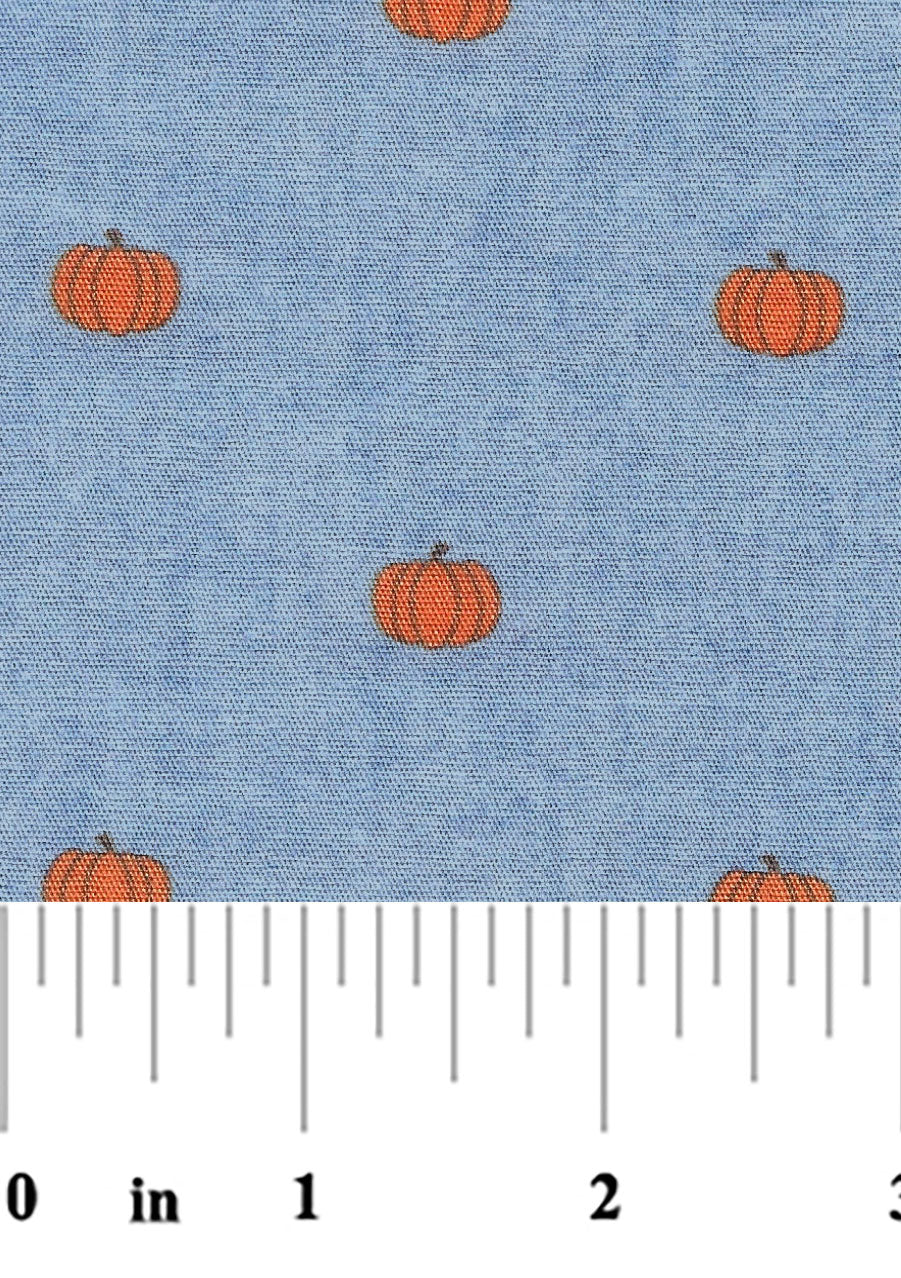 Blue chambray fabric with scattered small orange pumpkin print, fall seasonal pattern