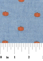Blue chambray fabric with scattered small orange pumpkin print, fall seasonal pattern