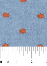 Blue chambray fabric with small scattered orange pumpkin print pattern