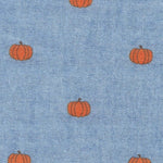 Blue chambray cotton fabric with scattered small orange pumpkin print pattern