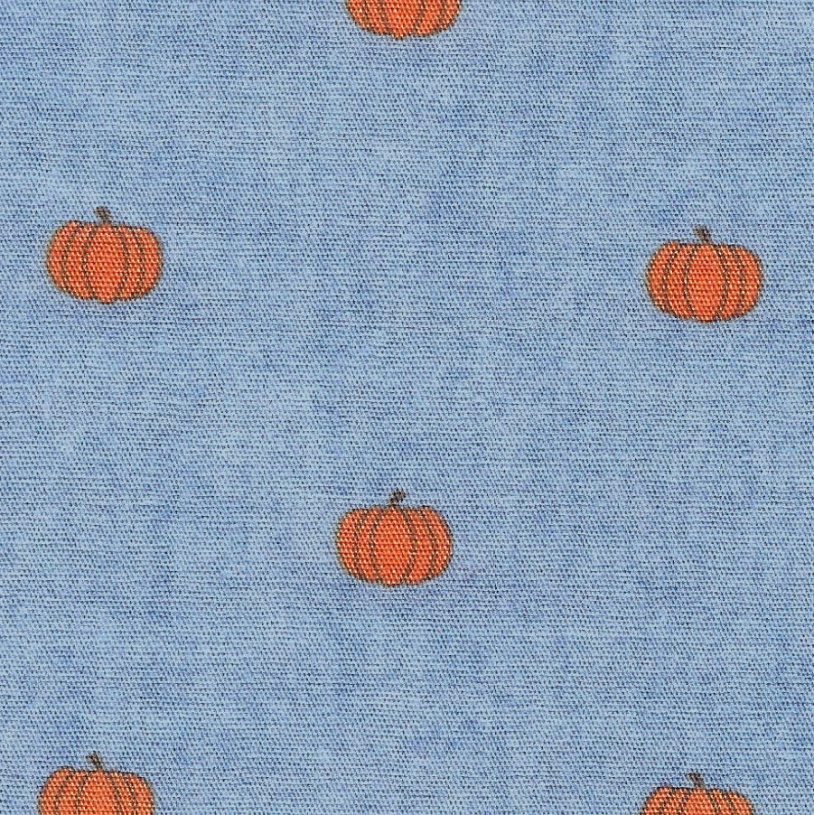 Blue chambray cotton fabric with scattered small orange pumpkin print pattern