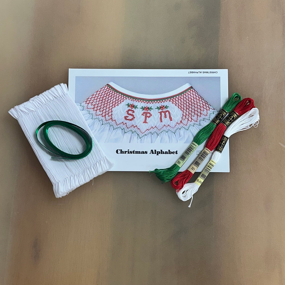 Christmas Alphabet smocking kit with pre-pleated white fabric, green ribbon, and red, green, white DMC floss