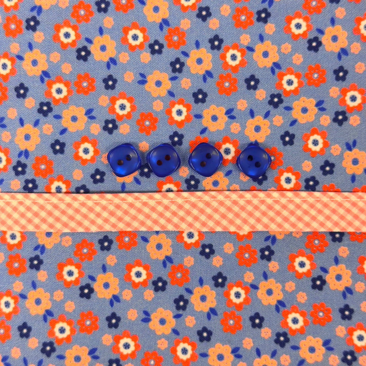 Blue floral fabric with orange flowers, four blue buttons, and pink gingham ribbon trim.