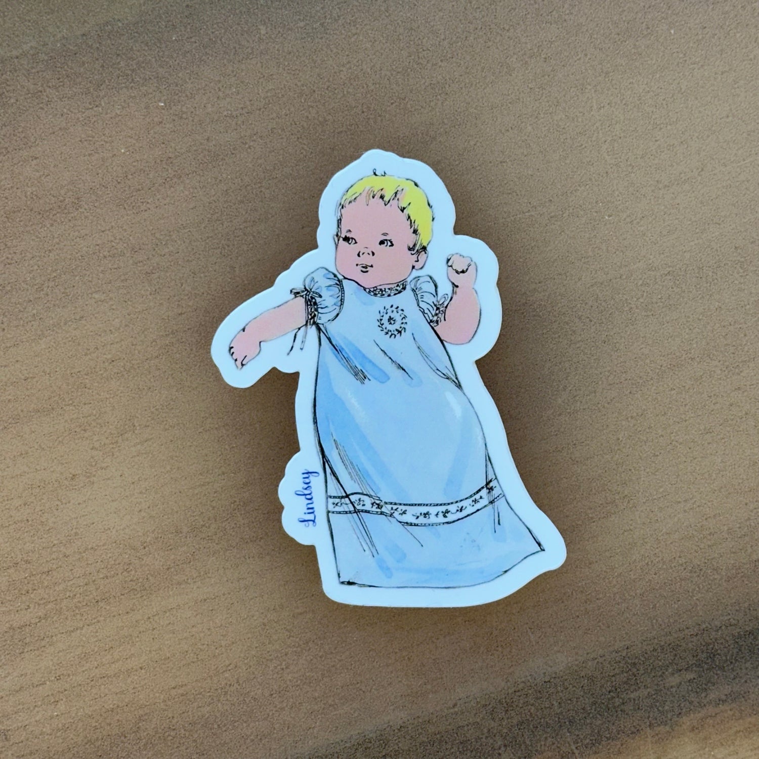 Vintage-style baby sticker in blue gown with blonde hair, signed Lindsey
