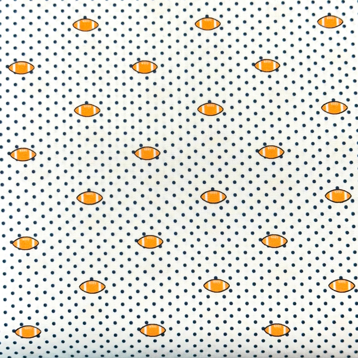 White fabric with navy polka dots and small orange football repeat pattern