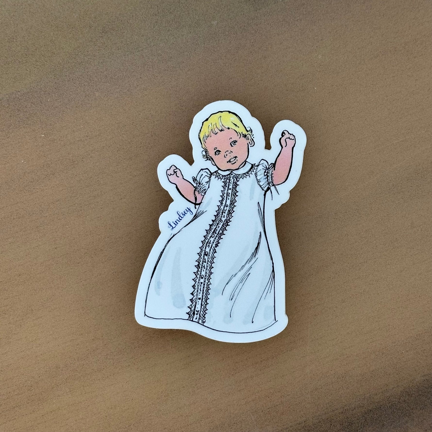 Lindsey vintage-style baby sticker featuring blonde infant in white christening gown