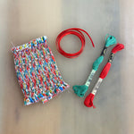 Smocked ornament kit with colorful Liberty fabric, red ribbon, and teal and red DMC floss