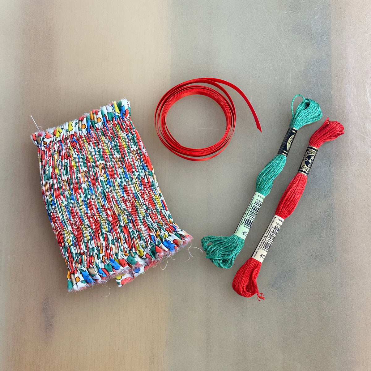 Smocked ornament kit with colorful Liberty fabric, red ribbon, and teal and red DMC floss