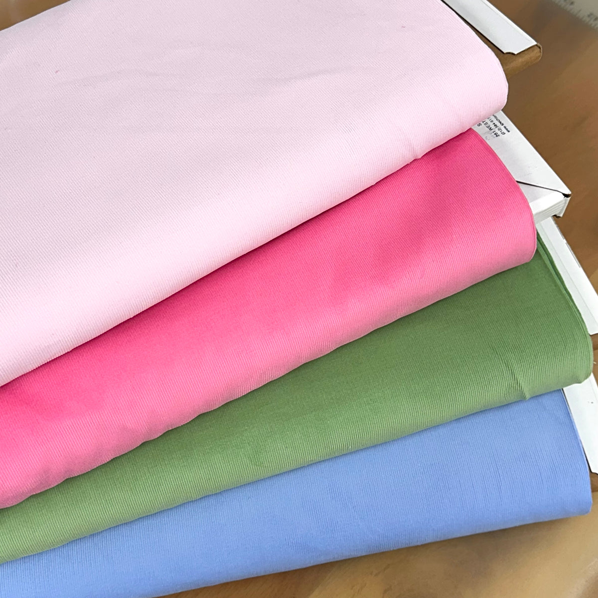 Folded solid corduroy fabric in pink, hot pink, sage green, and periwinkle blue