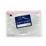 Clear pouch with pink zipper and 'project in progress' logo on a textured surface