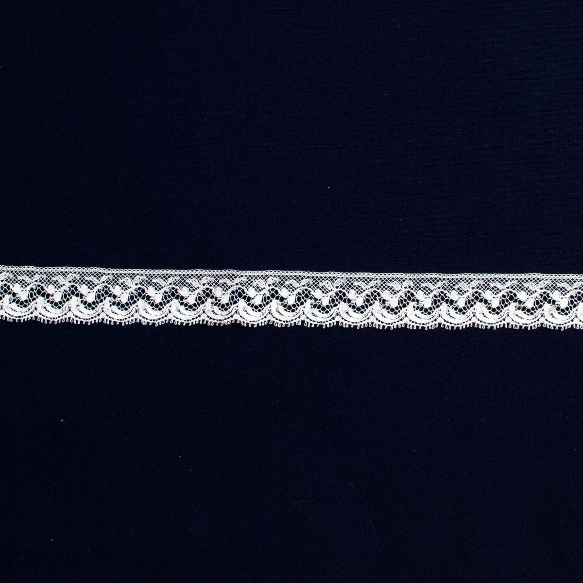 White scalloped lace edging trim with delicate floral pattern on navy background