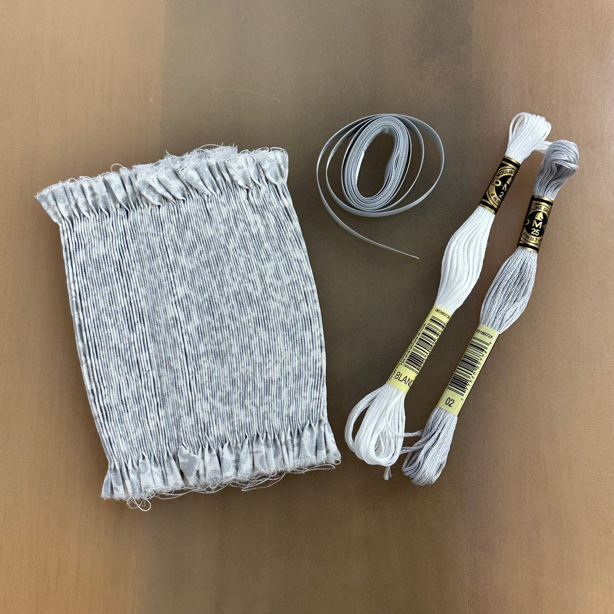 Metallic smocking kit with gray pleated fabric, elastic, and two DMC embroidery floss skeins