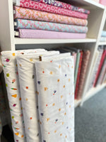 White seersucker fabric rolls with colorful fruit and vegetable prints, displayed in a fabric shop