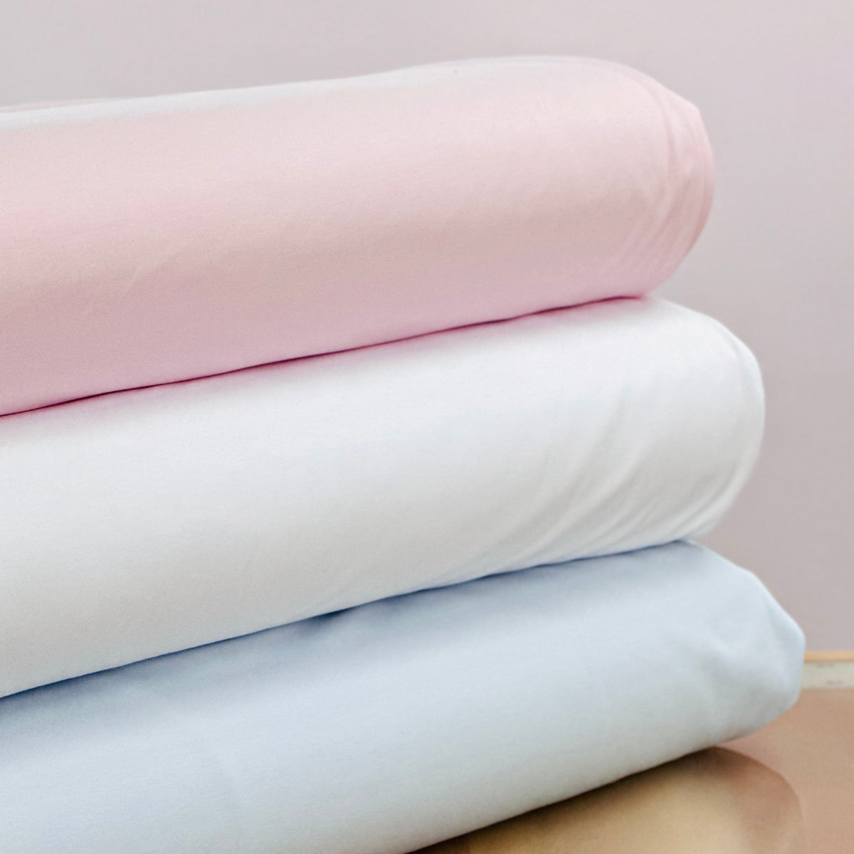 Three neatly folded knit fabric cuts in pink, white, and light blue stacked together