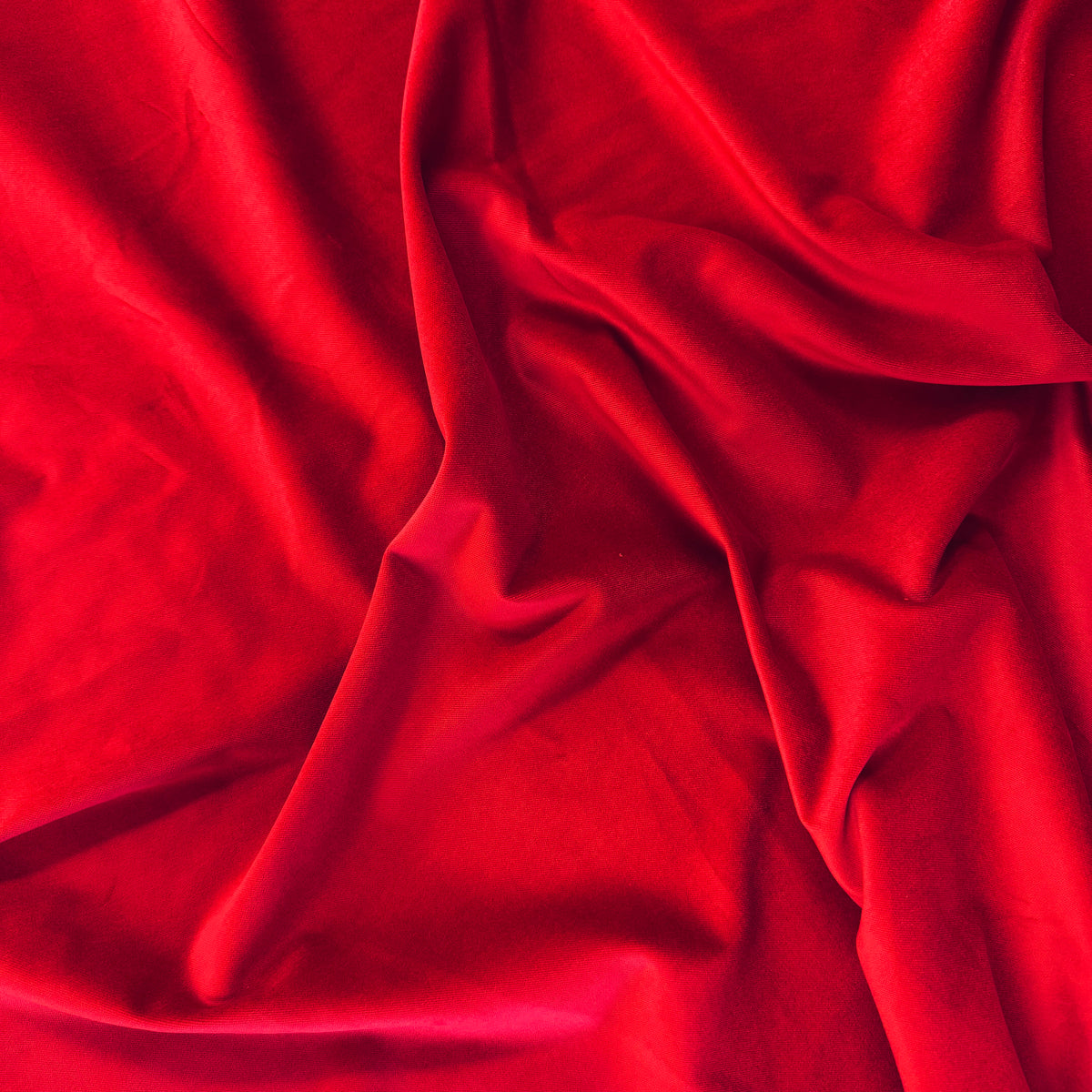 Red velveteen fabric with soft draping folds and a smooth, luxurious texture