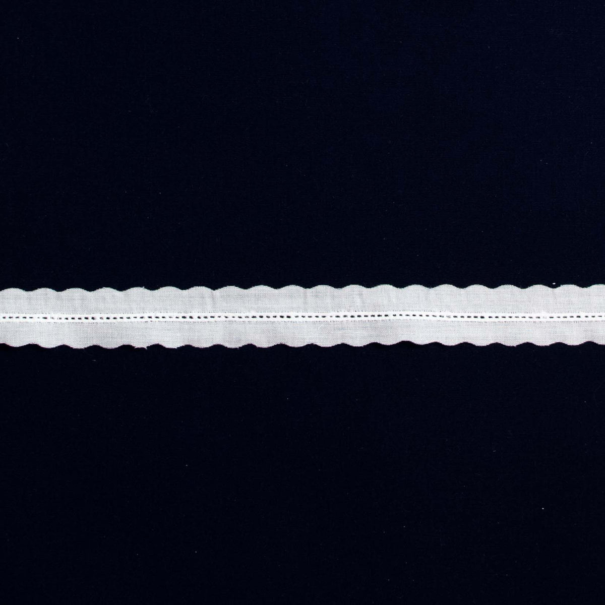 White cotton entredeux lace trim with scalloped edges on dark background