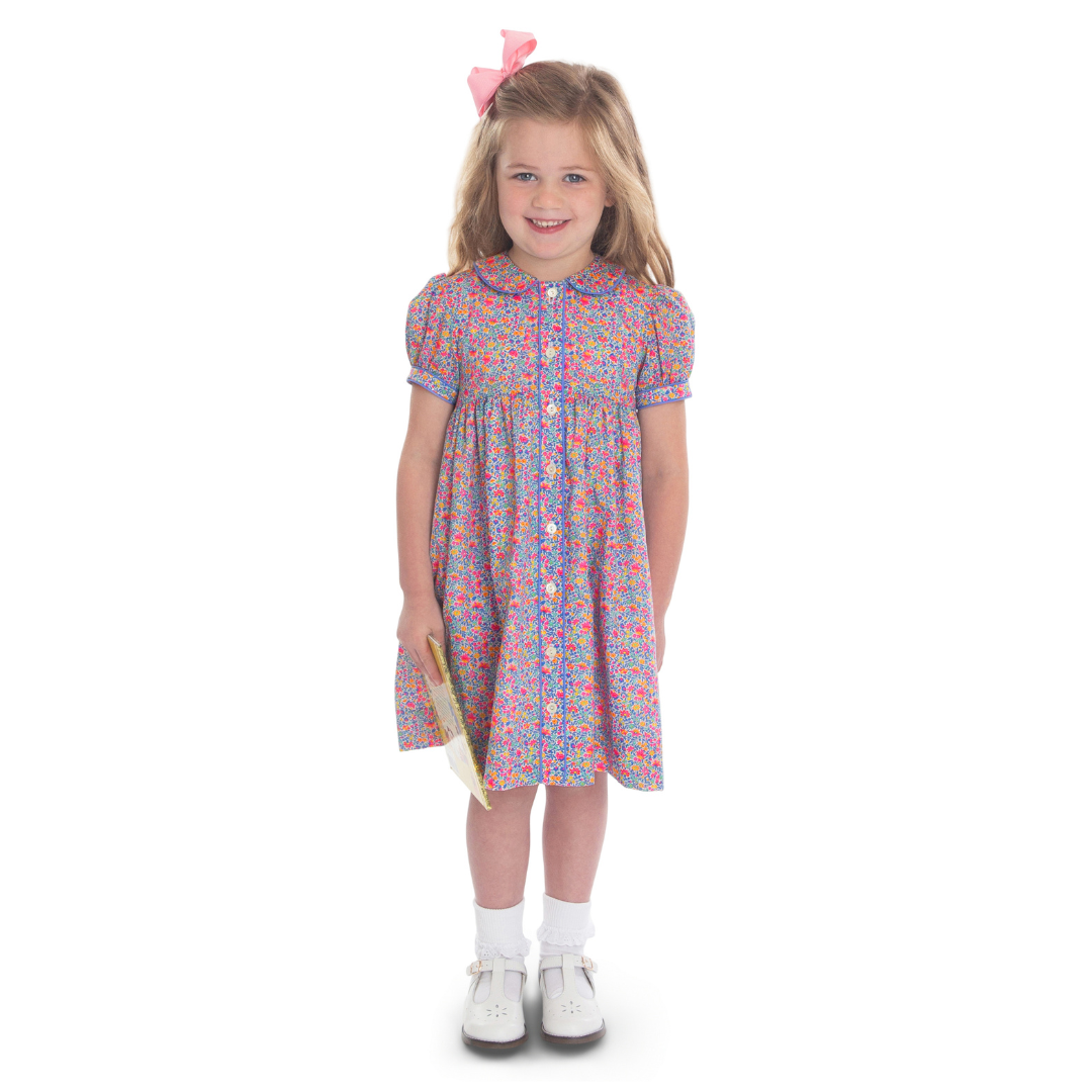 Girl wearing floral button-front dress with peter pan collar, puff sleeves, and pink hair bow