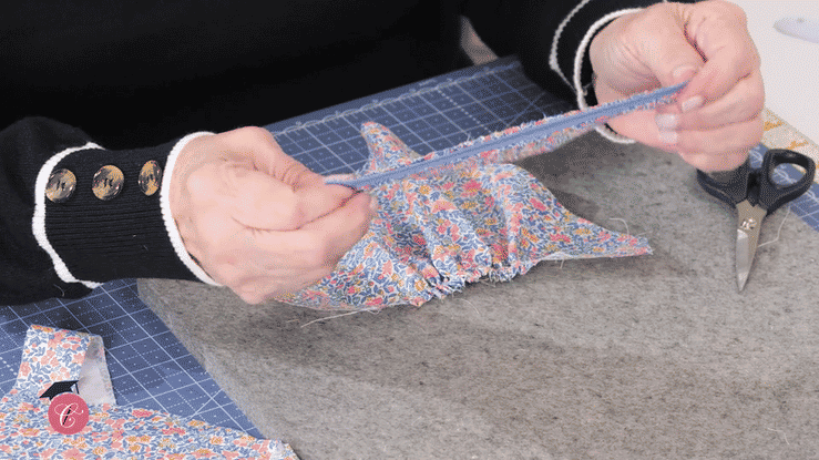Hands attaching blue bias tape to floral fabric on a cutting mat