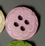 Pink plastic button with embossed flower petal design and four holes