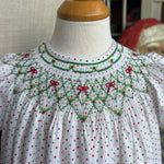 White blouse with red and green smocking  on a mannequin against a neutral background