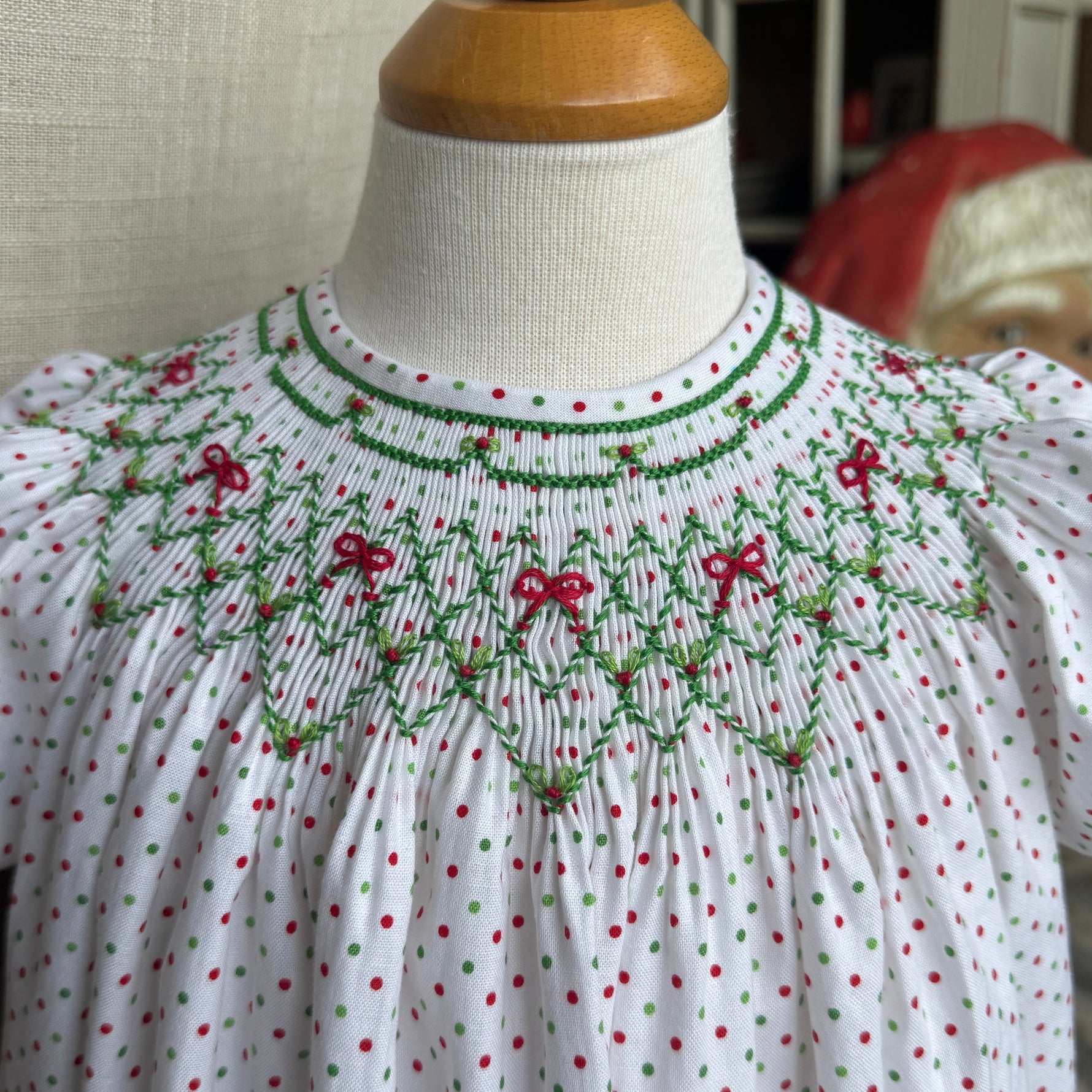 White blouse with red and green smocking  on a mannequin against a neutral background