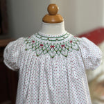 White dress with red polka dots and green smocking on a mannequin against a neutral background