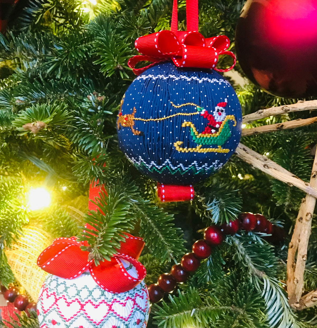 Navy smocked Christmas ornament with Santa sleigh design, red ribbon bow, on tree