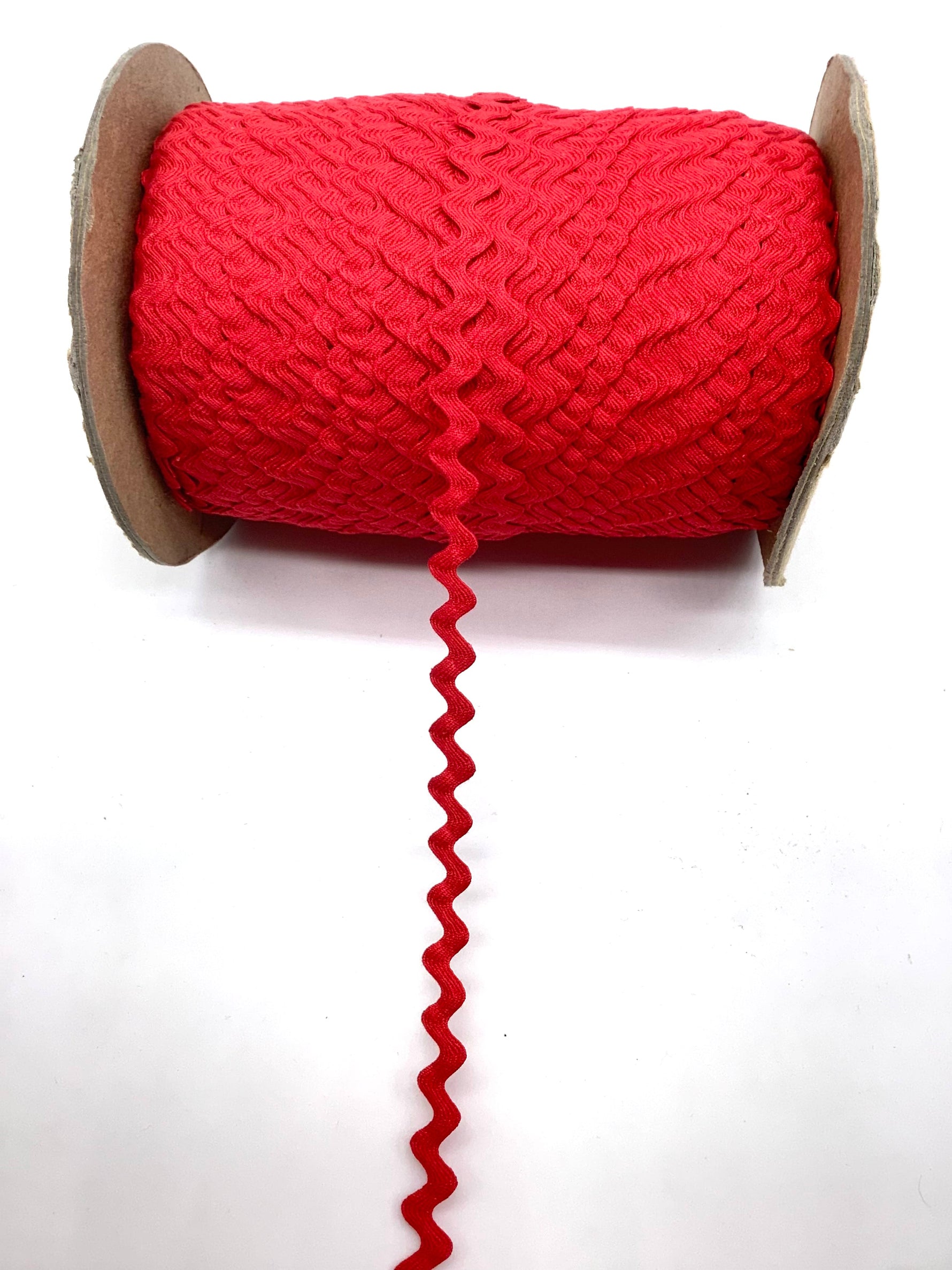 Red ric rac trim wound on a cardboard spool with loose zigzag end