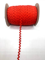 Red cotton ric rac trim on a cardboard spool with loose end trailing down