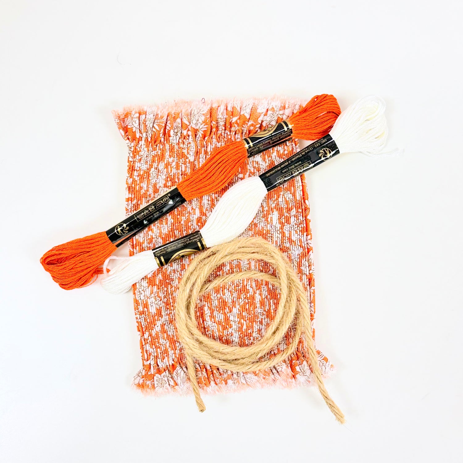 Orange and white smocked fabric with DMC embroidery floss skeins and natural jute twine