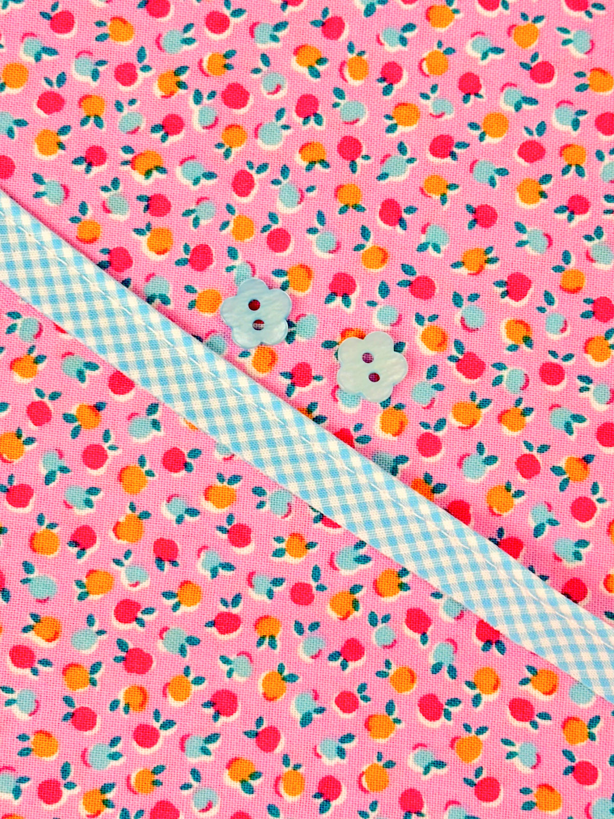 Pink floral fruit print fabric with blue gingham ribbon and two flower-shaped buttons