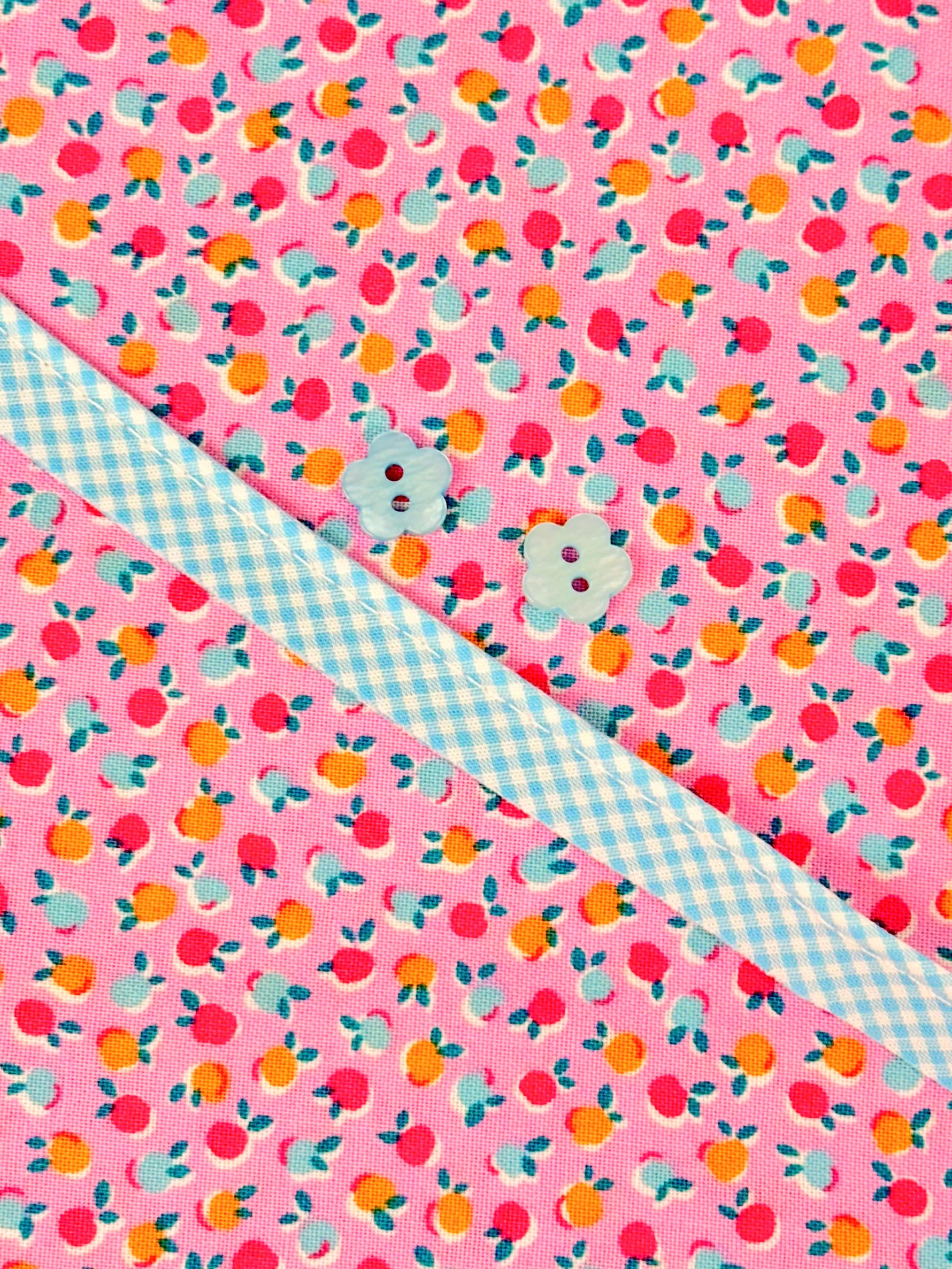 Pink floral fruit print fabric with blue gingham ribbon and two flower-shaped buttons