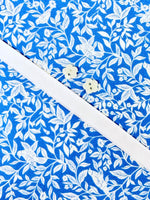 Blue floral cotton fabric with white leaf print and two small flower-shaped buttons