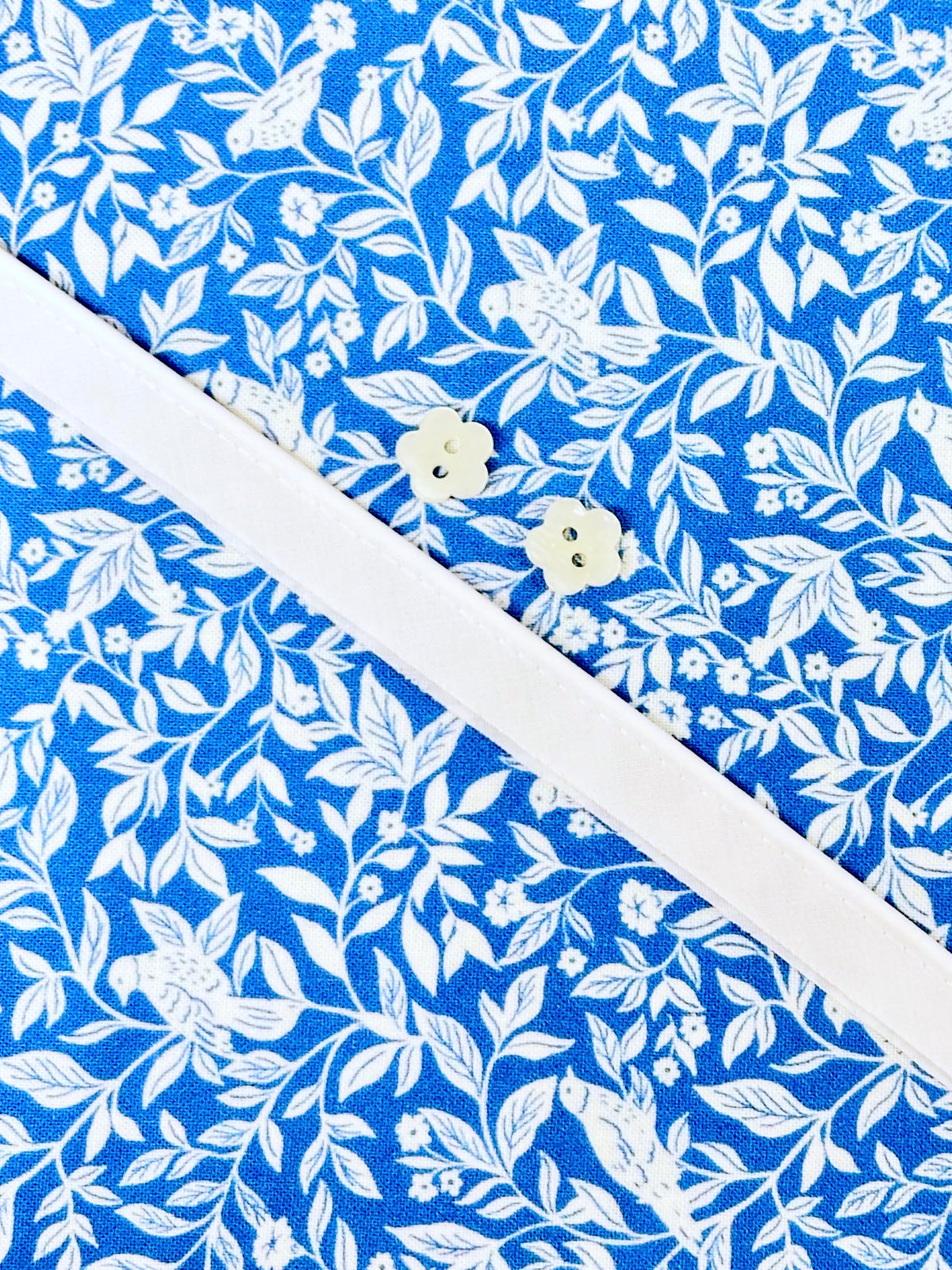 Blue floral cotton fabric with white leaf print and two small flower-shaped buttons