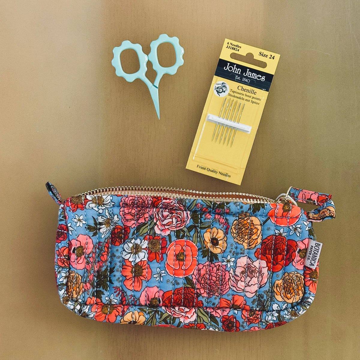 Floral quilted zip pouch, mint scissors, and John James size 24 chenille needles flatlay