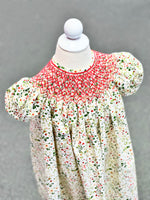 Smocked bishop dress in cream floral print with red smocking on child mannequin